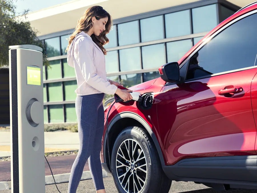 a person pluging in a red hybrid suv