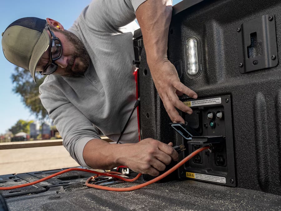 Man plugging a power cord into the onboard generator outlet in the bed of a Ford F-150.