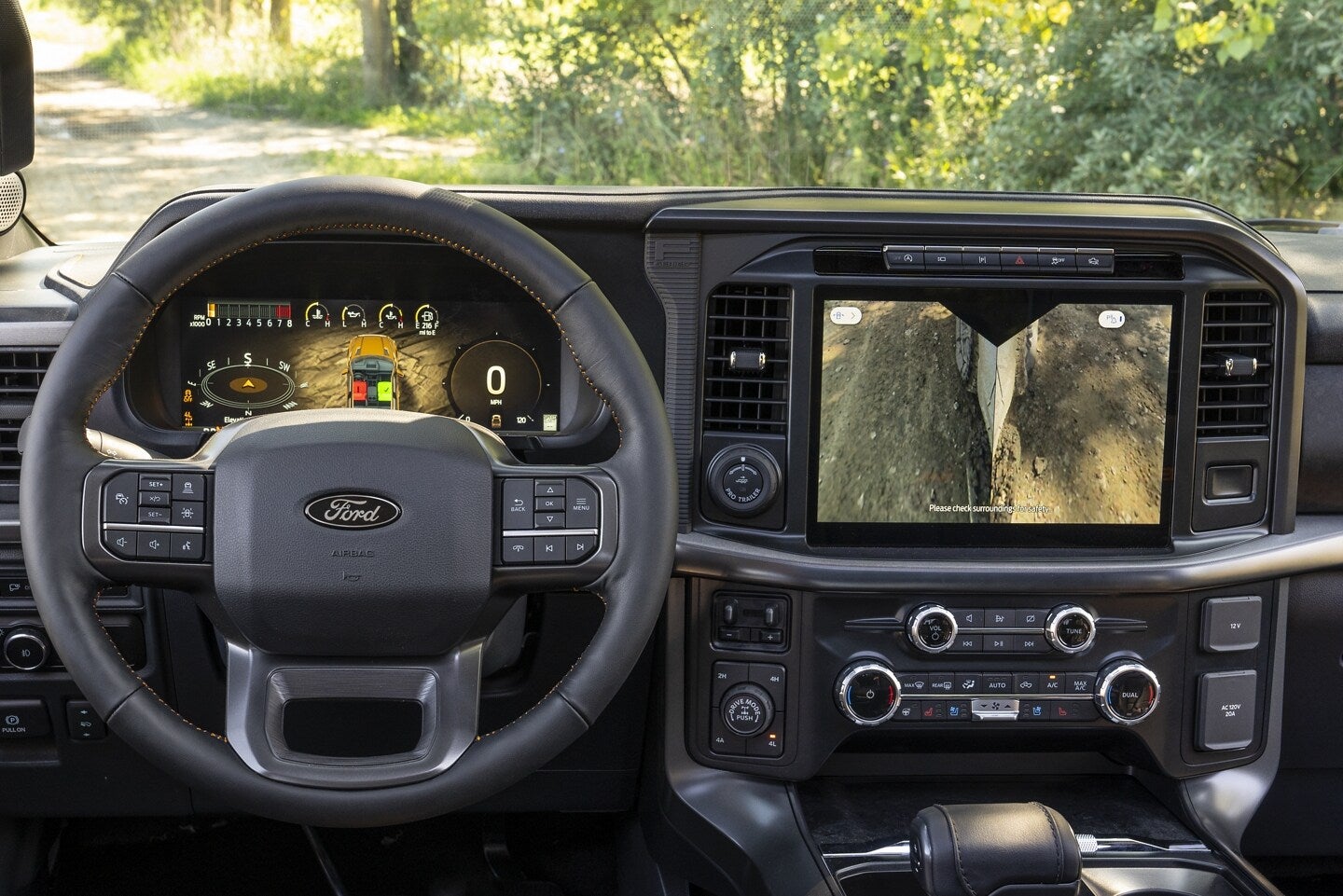 Ford F-150 interior featuring a steering wheel, digital instrument cluster, and a large touchscreen displaying a rearview camera feed.