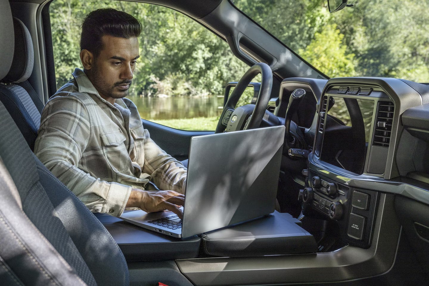Man working on a laptop in the interior of a Ford F-150, using the center console workspace.