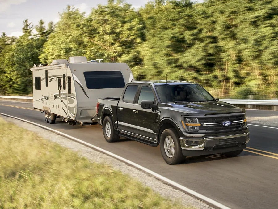 Black Ford F-150 towing a camper on a scenic road with trees along the sides.