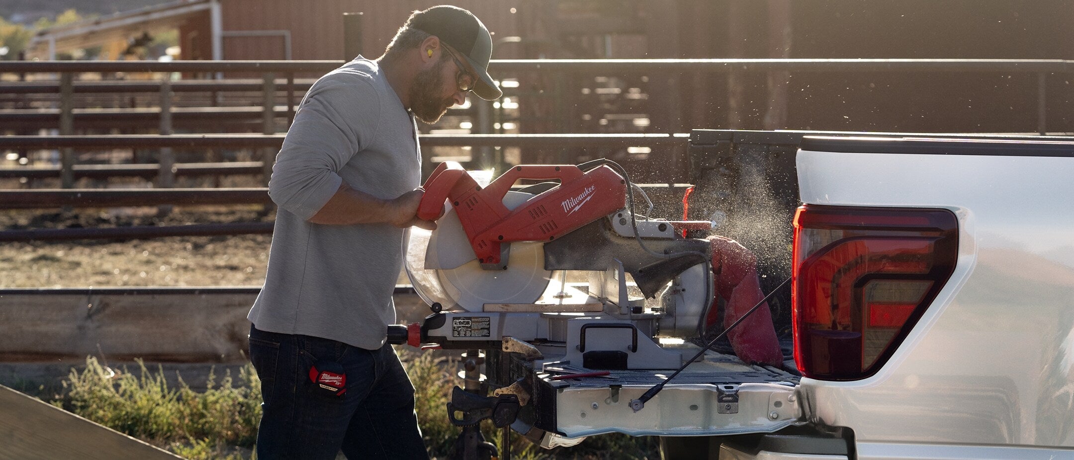 Worker using a circular saw on the tailgate of a Ford F-150 parked on a farm.