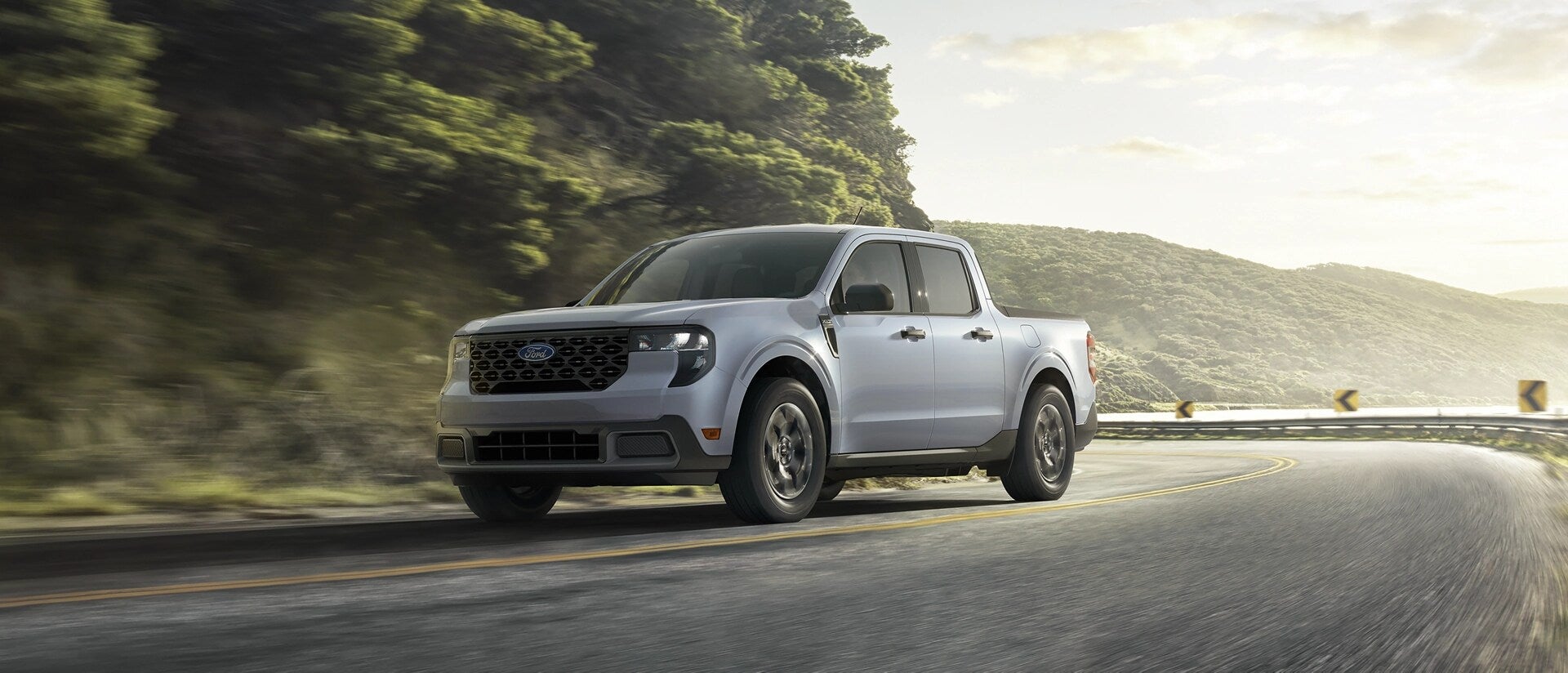 a gray ford maverick driving on a paved road with a scenic background