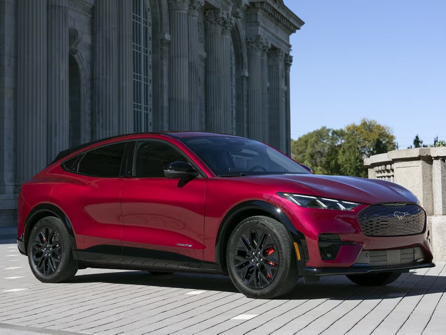 2025 Ford Mustang Mach-E in red, parked in front of a historic building.