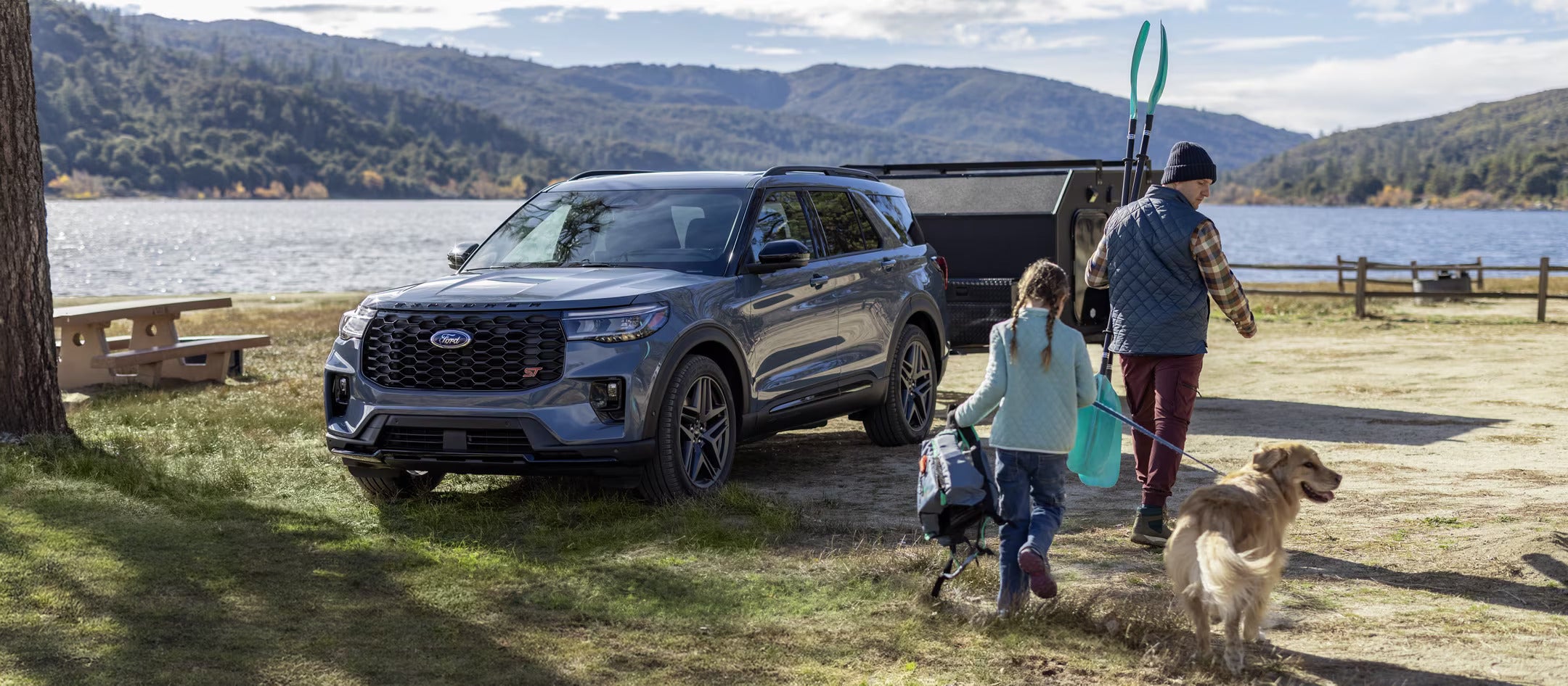 Family walking with their dog near a 2025 Ford Explorer parked by a lake.