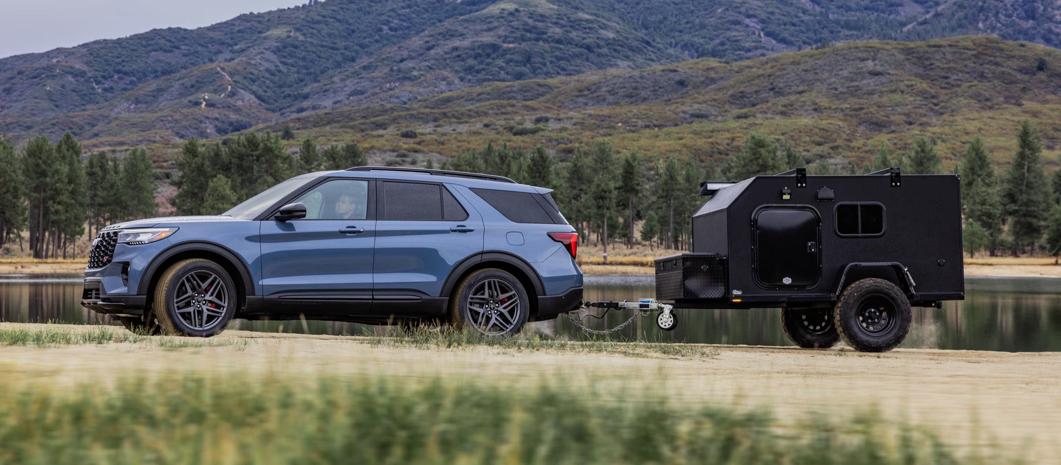 2025 Ford Explorer towing a small trailer in a scenic mountainous area.