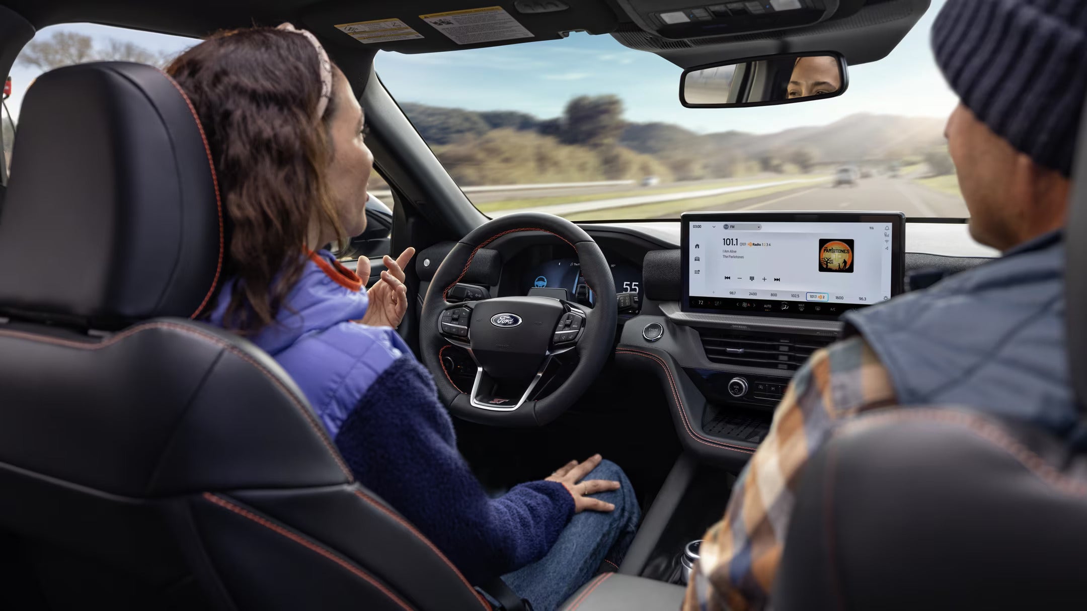 Interior view of the 2025 Ford Explorer showing two people driving with touchscreen and dashboard in focus.