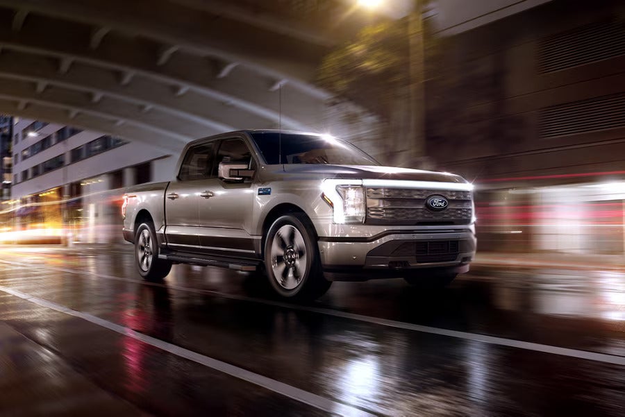 Ford F-150 Lightning driving through a city at night, showcasing electric vehicle performance in an urban setting.
