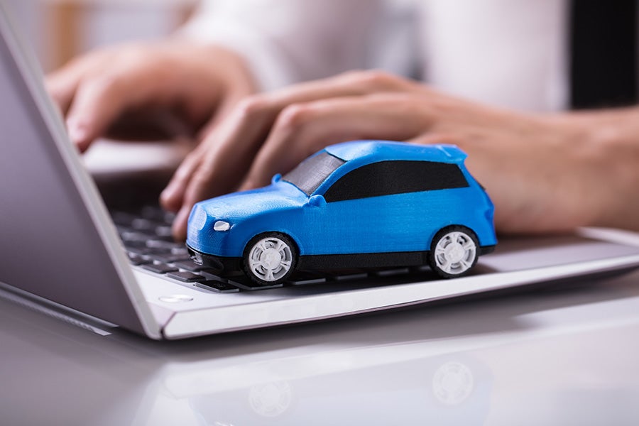 a blue car sitting on a laptop with a persons hands typing