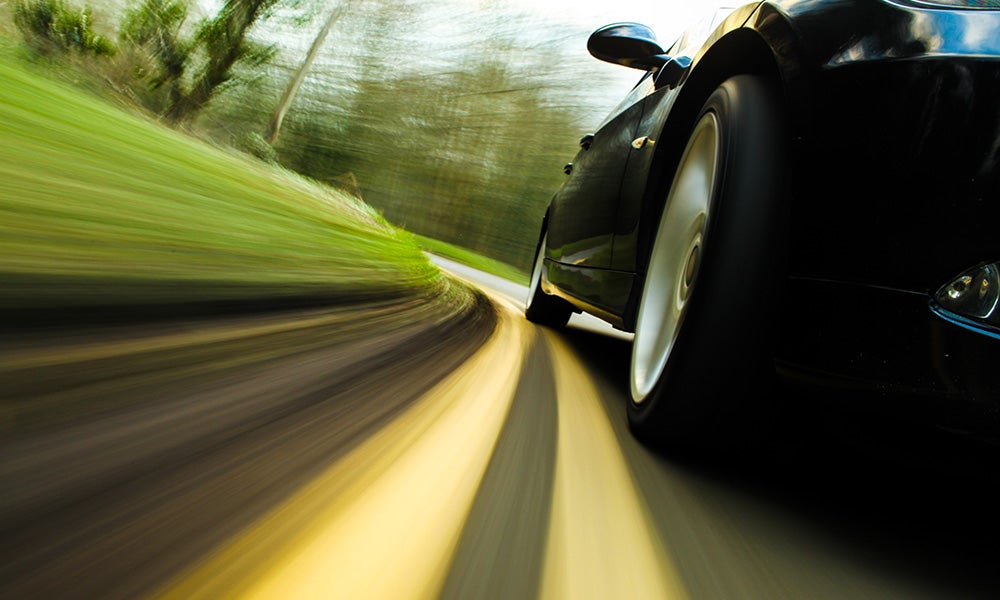 a dark car speeding on a paved road with in the country side