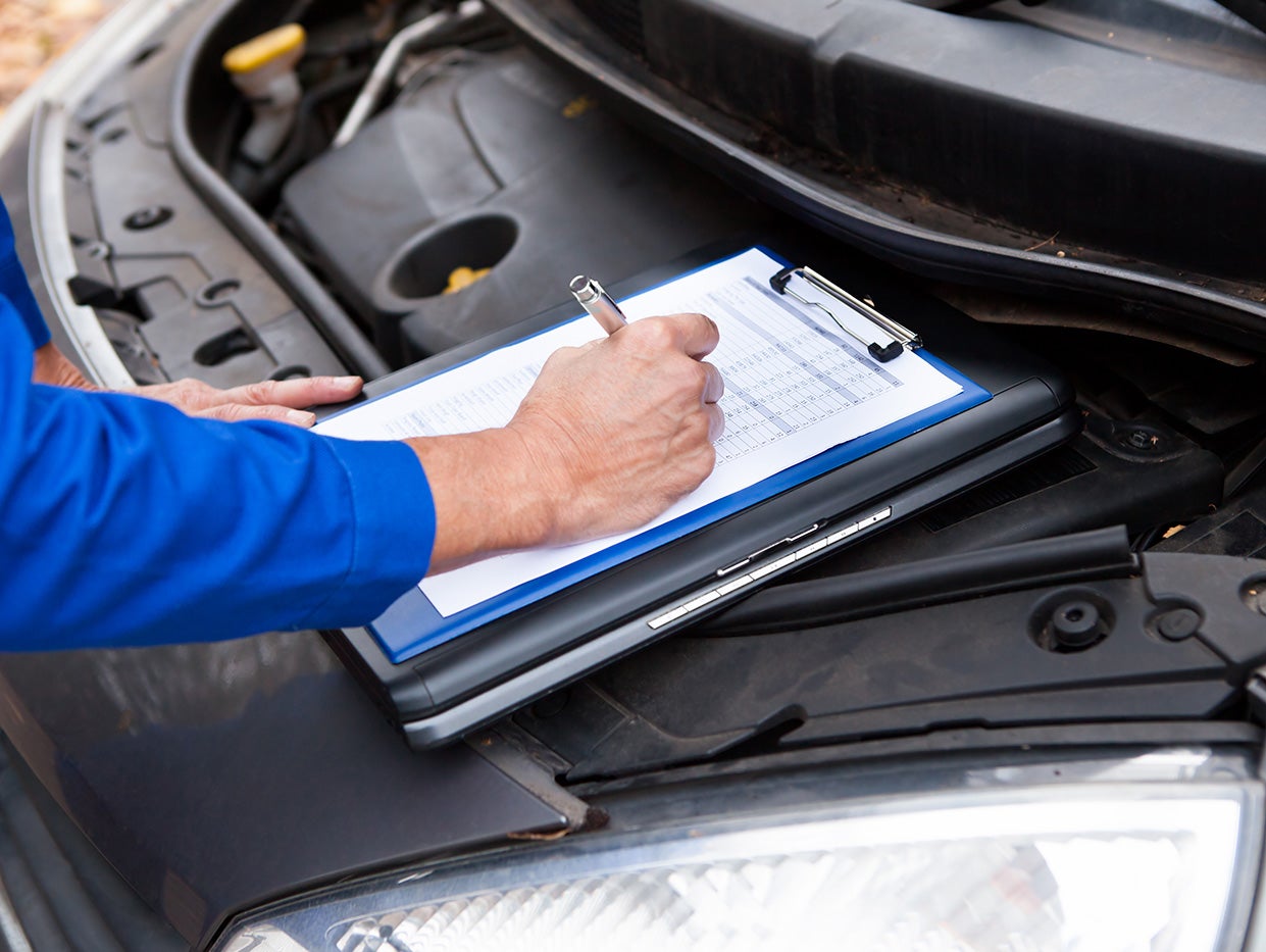 a service tech with a clip board and pen inspection the engine of a vehicle
